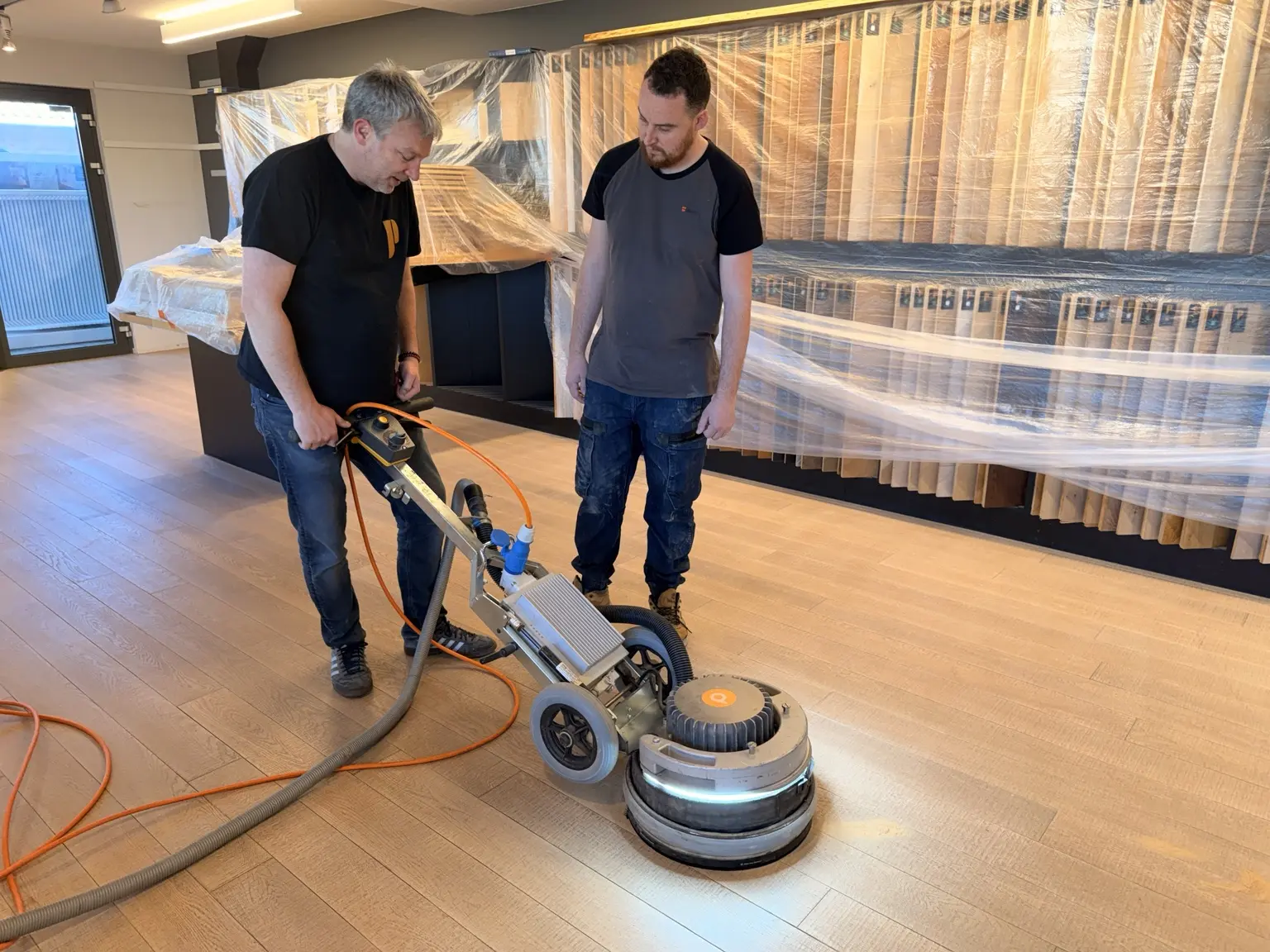 Deux professionnels des Ponceurs Réunis règlent et utilisent une ponceuse de sol dans le showroom